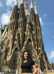 woman with long black hair standing in front of a tall cathedral